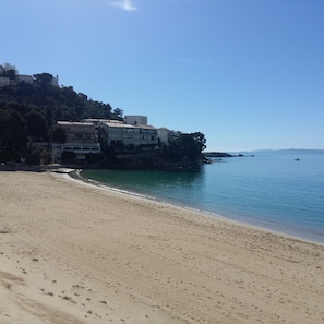 A sandy beach with buildings on a cliff overlooking the sea.