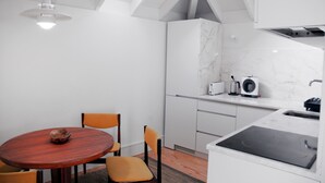 Une cuisine moderne avec des meubles blancs, un pare-feu en marbre, une table ronde en bois et deux chaises orange.