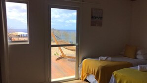 A room with two beds, a large sliding glass door to a deck, and a view of the beach. - Pousada Solar do Pico (Fernando de Noronha)
