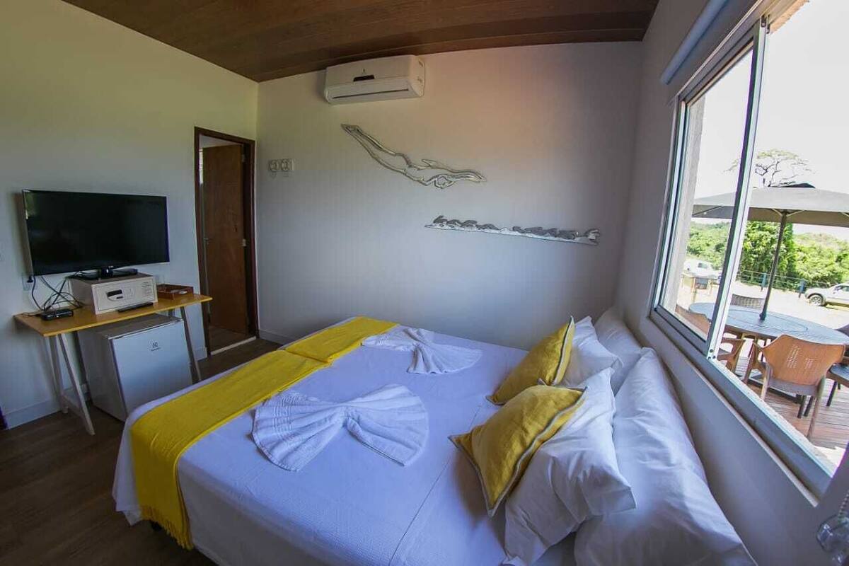 A hotel room with a bed, a TV, a small desk, and a window with a view of the outside.