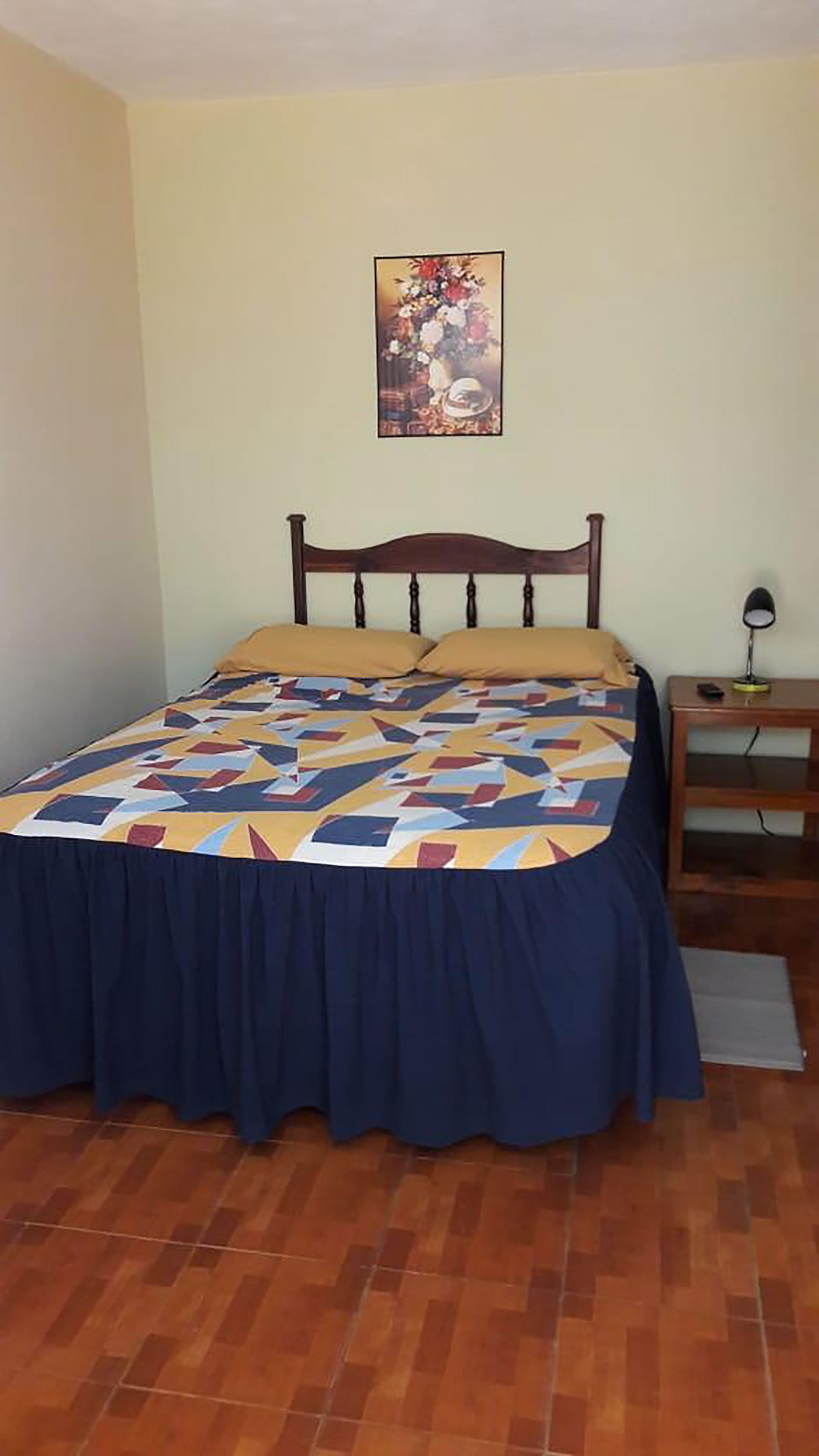 A bedroom with a bed, a nightstand, a lamp, and a painting on the wall.