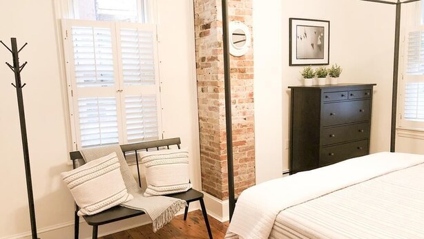 A bedroom with a four-poster bed, a bench with cushions, a coat rack, a dresser, and a brick wall. - 2 Blocks to Mall - 8 Minute Walk to Beach (Cape May)