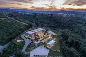 Una casa moderna con piscina, rodeada de exuberante vegetación y montañas al fondo.