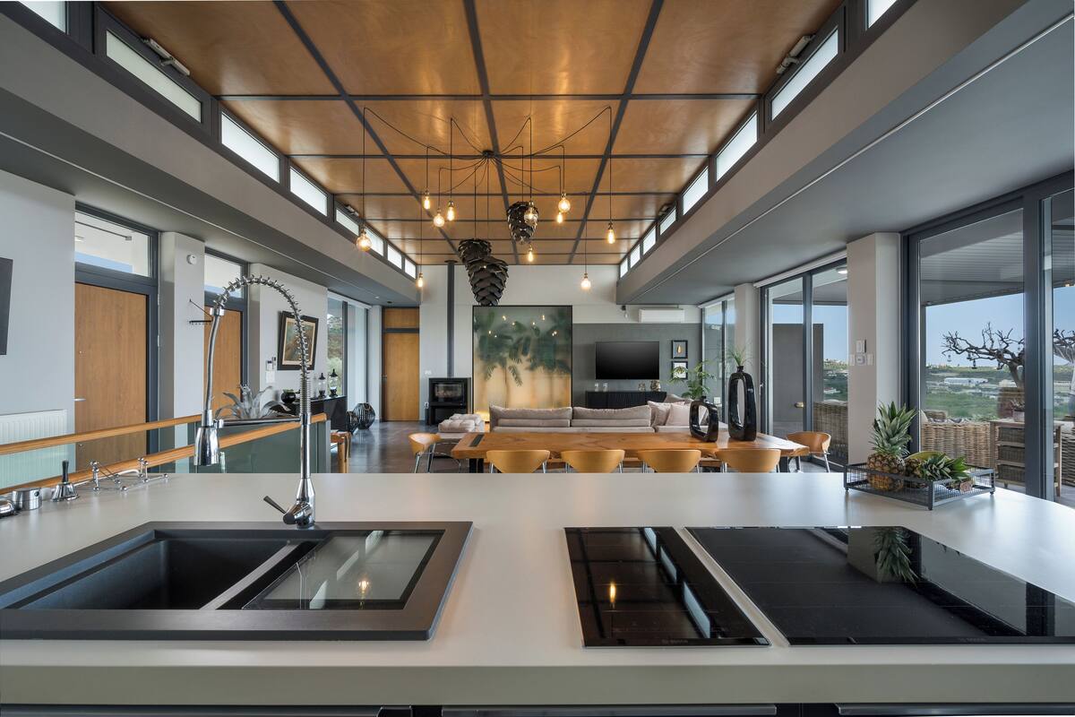A modern kitchen with a central island, large windows, and a dining area with a sofa and chairs.