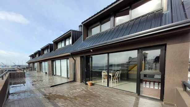 A modern building with a flat roof, large glass windows, and a wooden deck. - Gente del Sur - Rivadavia (Ushuaia)