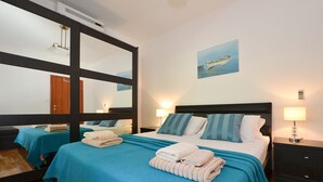 Een hotelkamer met een grote spiegel, een bed met blauw-witte beddengoed, een schilderij van een boot aan de muur en een nachtkastje met een lamp.