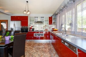 Een moderne keuken met rode kastjes, een marmeren vloer en een groot raam met kantgordijnen.