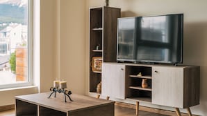 Una sala de estar moderna con un televisor de pantalla plana grande sobre un mueble de madera, una mesita con velas y vistas a edificios a través de una ventana.