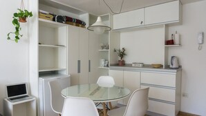 Una cocina compacta con armarios blancos, una mesa de comedor de cristal y sillas blancas.