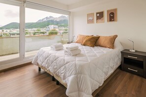 Un dormitorio con una cama grande, una mesita de noche, una lámpara y vistas a montañas a través de un ventanal amplio.