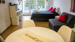 Una habitación con cama, sofá, mesa y ventana con vista a árboles.