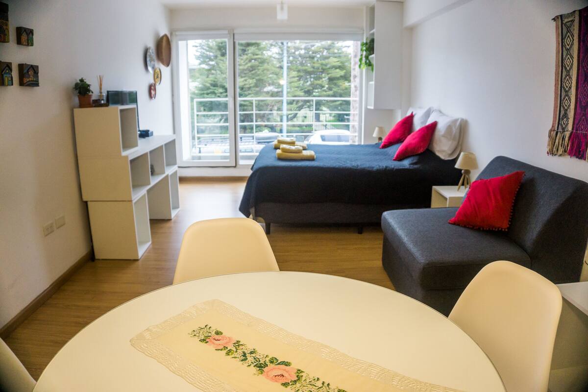 Ein Zimmer mit Bett, Sofa, Tisch und Fenster mit Blick auf Bäume.