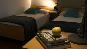 Une chambre d’hôtel avec deux lits simples, une table de chevet avec une lampe, un livre et une pomme.