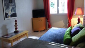 A bedroom with a bed, a television on a wooden cabinet, a window with red curtains, and a lamp on a bedside table. - HOUSE 4/5 PEOPLE LA ROCHELLE (La Rochelle)