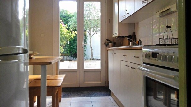 A kitchen with white cabinets, a built-in oven, and a dining area with a bench and table. - HOUSE 4/5 PEOPLE LA ROCHELLE (La Rochelle)