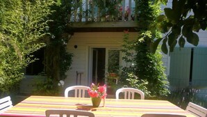 A patio with a striped table and white chairs, surrounded by greenery and a building with a balcony. - HOUSE 4/5 PEOPLE LA ROCHELLE (La Rochelle)