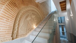 A modern staircase with intricate brick and plaster detailing, leading to a second-floor area with glass railings and a view of the interior space. - Hommyhome Casa Assle 101 (Sevilla)
