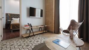 A hotel room with a bed, a TV mounted on the wall, a small wooden table with a magazine, and a chair. - Hommyhome Casa Assle 101 (Sevilla)