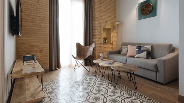 A modern living room with a sofa, a coffee table, a chair, and a TV mounted on the wall. - Hommyhome Casa Assle 101 (Sevilla)