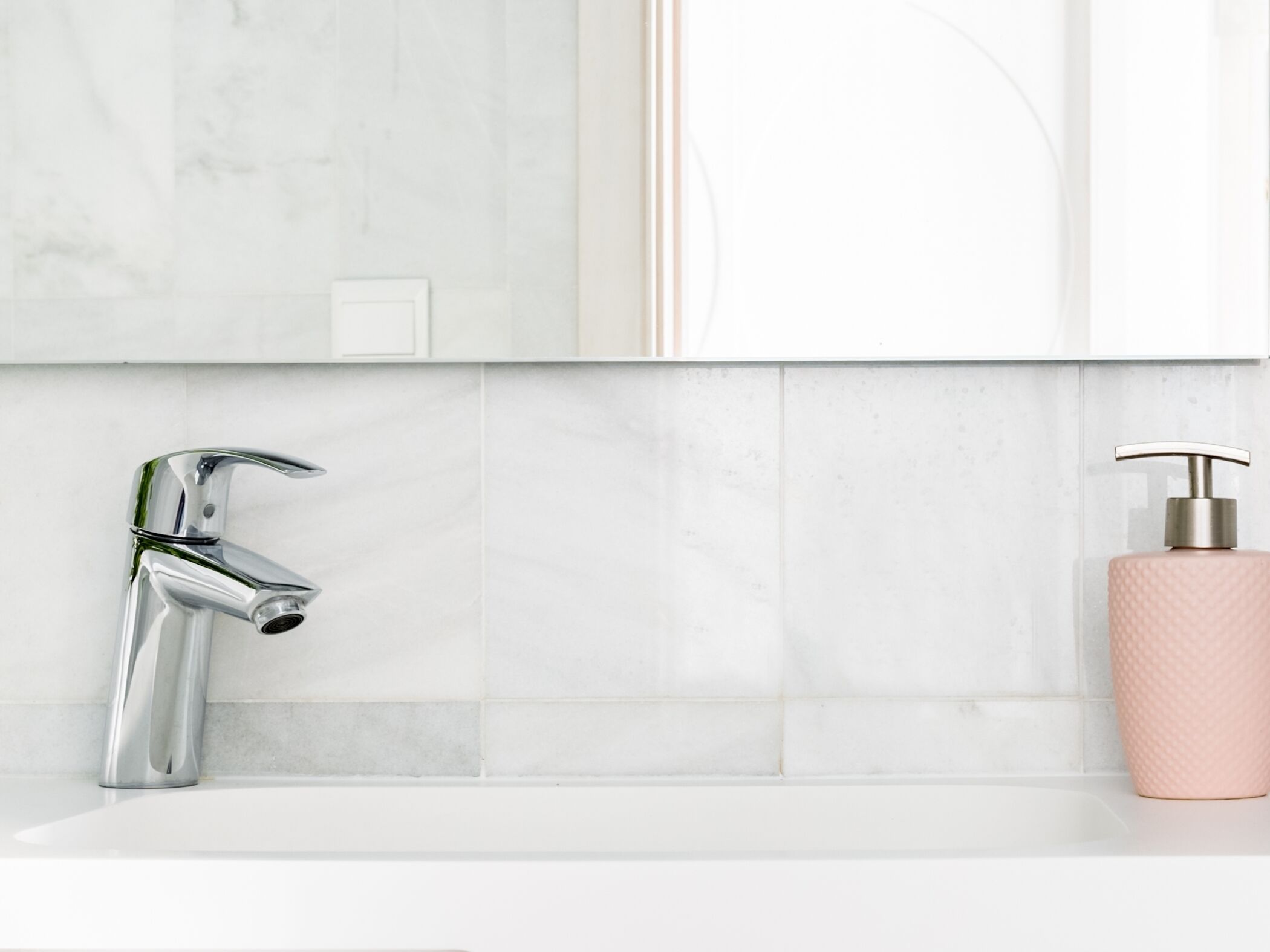 Un baño con grifo cromado, lavamanos blanco y dispensador de jabón rosa.
