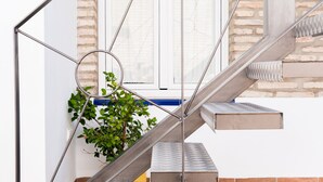 Un escalier avec des rampes en métal et un pot de fleurs placé à côté.