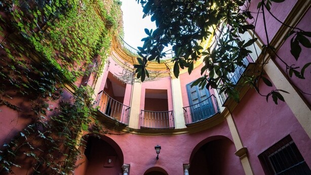 Un patio con paredes rosadas, arcos y balcones con barandillas.