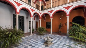 Un patio con piso a cuadros, arcos rojos y blancos, y una fuente en el centro.