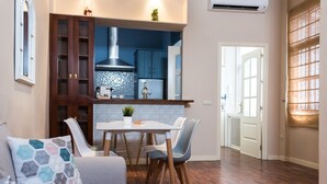 Una cocina moderna con armarios azul oscuro, una mesa de comedor blanca y un sofá gris con cojines estampados.