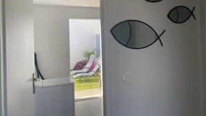 Une pièce avec une porte blanche, un décor mural représentant des poissons, et un aperçu d’un espace extérieur avec une chaise et des fleurs.