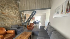 Un salon moderne avec un mur en pierre, des canapés en cuir, une table basse en bois et un escalier menant à un niveau supérieur.