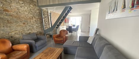 A modern living room with a stone wall, leather sofas, a wooden coffee table, and a staircase leading to an upper level.