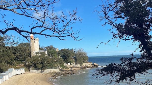Une plage avec une tour, un rivage rocheux et des arbres.