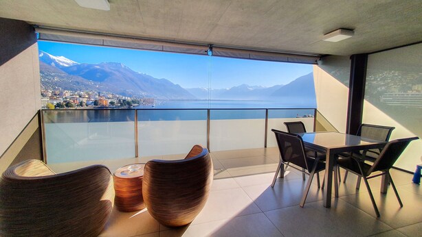 Een balkon met uitzicht op een meer en bergen, voorzien van stoelen en een tafel.
