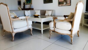 Een zithoek met twee witte fauteuils met houten frames, een witte salontafel en een bank op de achtergrond.