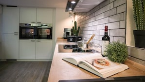 Una cocina moderna con armarios blancos, horno integrado, cafetera y una planta de cactus.