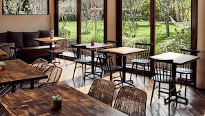 Un espace de restauration intérieur avec des tables et des chaises en bois, de grandes fenêtres donnant sur un jardin et des montagnes.