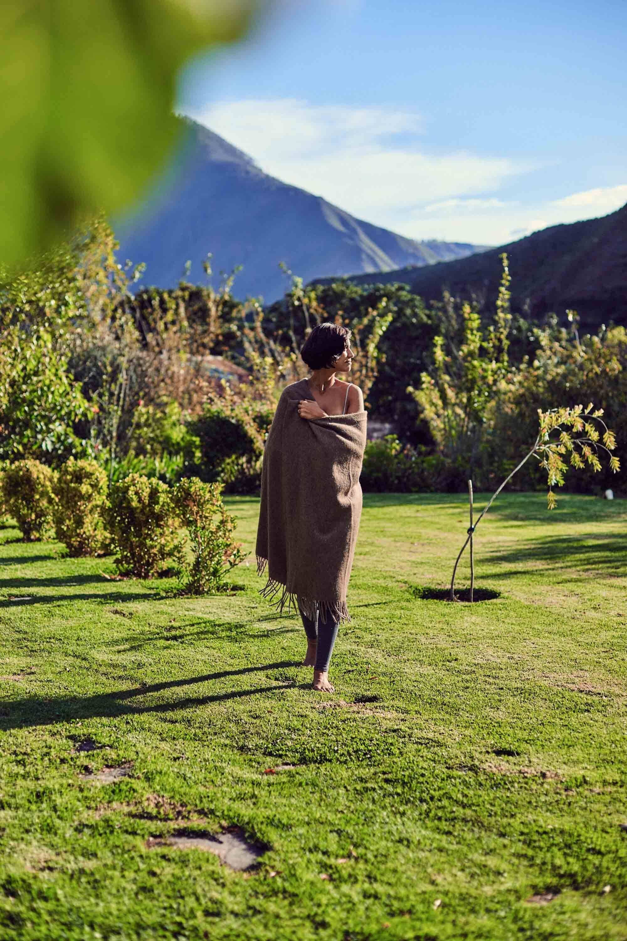 A person walking on a grassy path in a garden with a mountain in the background.