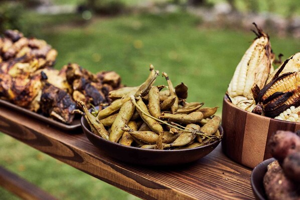 A wooden table with various roasted vegetables and corn on the cob. - Andenia Boutique Hotel, Sacred Valley (Calca)