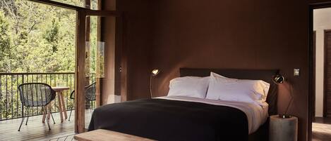 A bedroom with a large bed, a wooden bench, a small table, and a balcony with chairs.