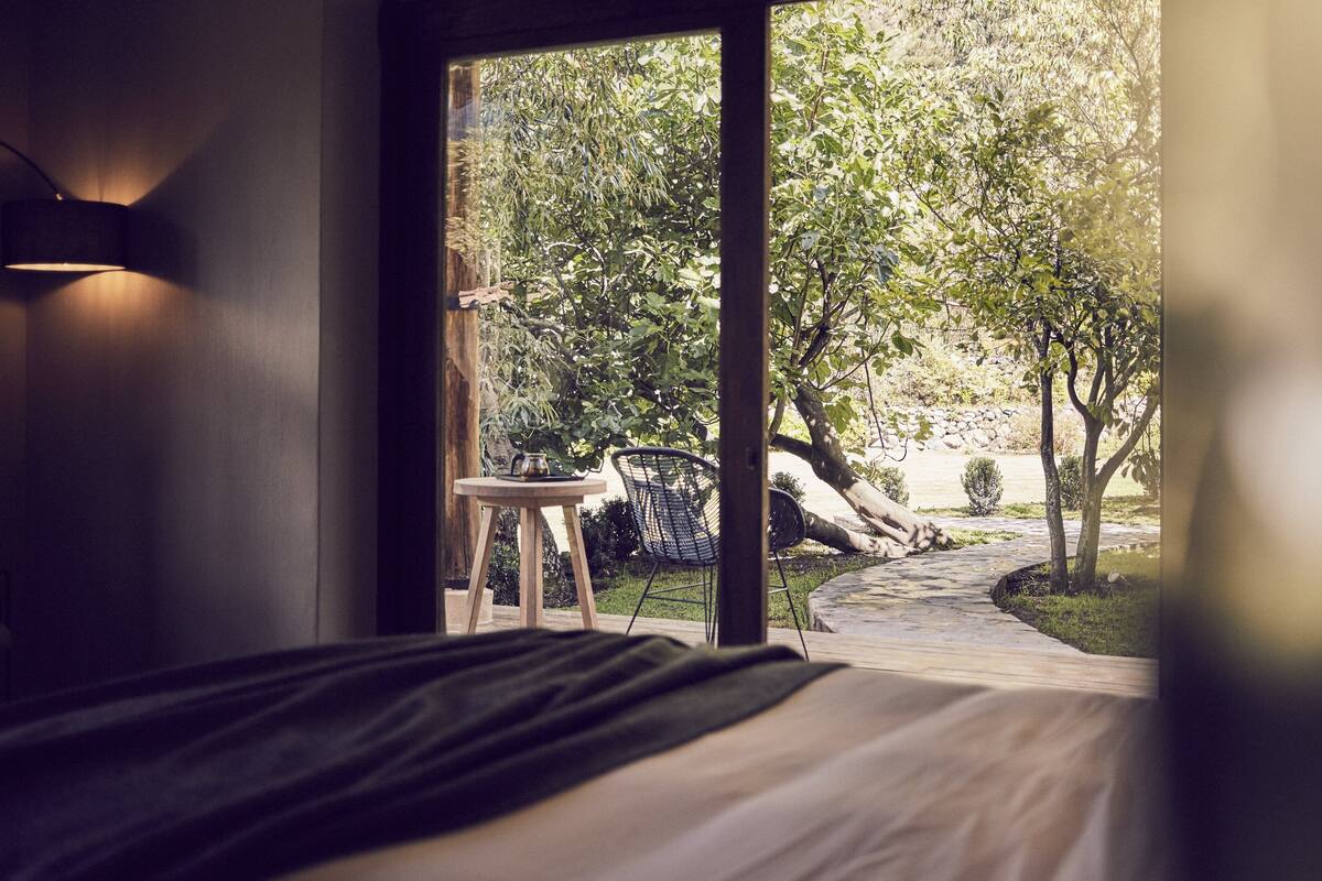 A bedroom with a large window, a bed, a small table, and a chair.
