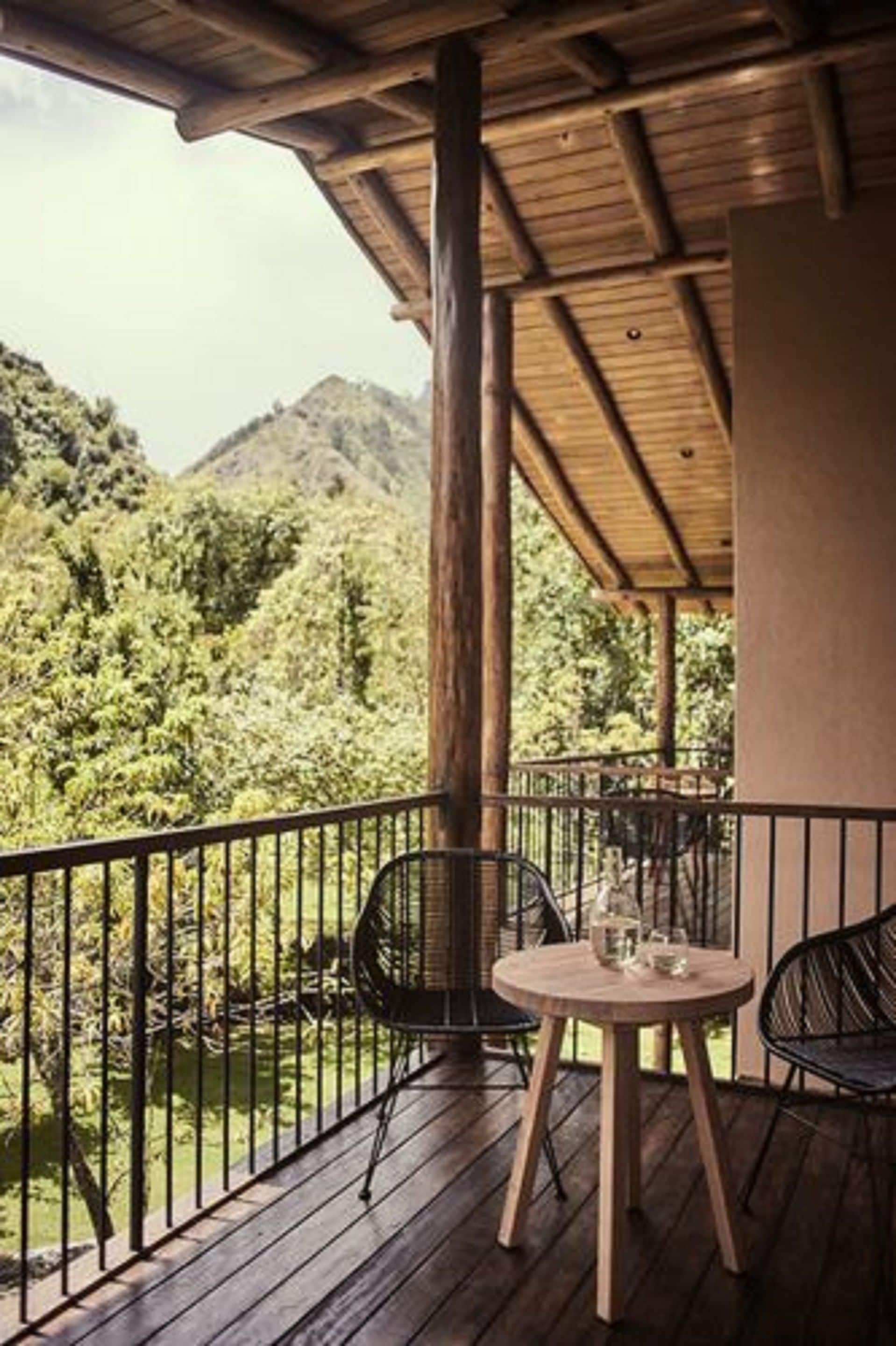 A wooden deck with a table and chairs, overlooking a lush green landscape with mountains in the background.