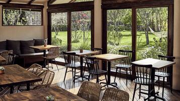 An outdoor dining area with wooden tables and chairs, a sofa, and a view of a garden.