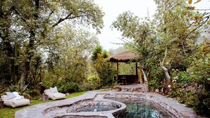 Un bain à remous en pierre, entouré d’une végétation luxuriante et abrité sous une structure à toit de chaume.