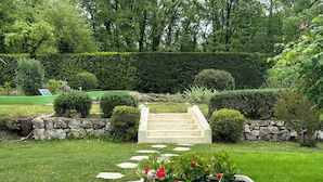 Un jardin avec un chemin de pierres menant à un escalier, entouré de haies soigneusement taillées et de diverses plantes.