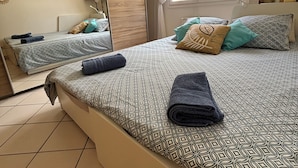 Une chambre avec un grand lit, une armoire, un miroir et une fenêtre avec des rideaux.