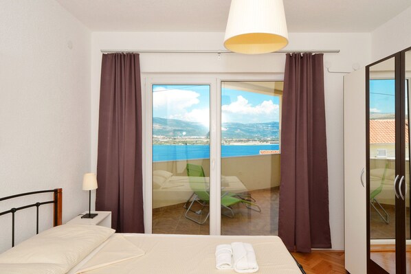 A bedroom with a bed, a nightstand, a lamp, and a view of a balcony with chairs and a table.