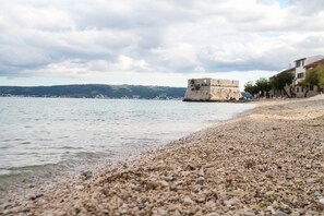 Ein Kiesstrand mit einer historischen Festung und Gebäuden entlang der Küste.