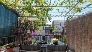 Eine Terrasse im Freien mit Frühstückstisch, umgeben von einem Bambuszaun und blühenden Pflanzen.