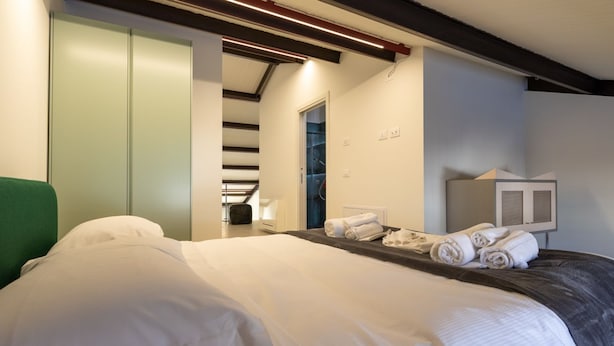 A neatly made bed with white linens, a green headboard, and a bedside table with rolled towels. - Rivadige Suite 4 with beautiful view on the river (Verona)
