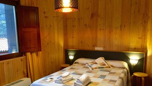 Une pièce aux murs lambrés, comprenant un lit, deux lampes de chevet, une fenêtre et un radiateur fixé au mur.